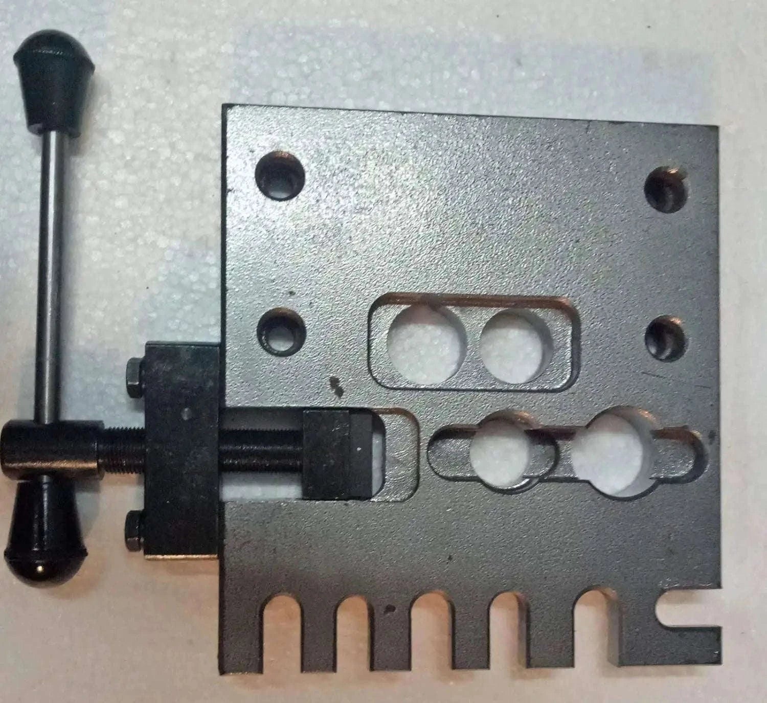 Gray metal holding plate fixture with bolt holes and central cutout